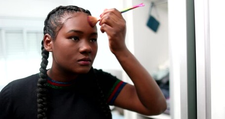 Black girl applying make-up in front of mirror. Young African woman applies makeup casual