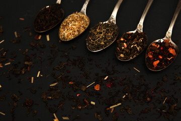 Various types of herbal tea in spoons. Spoons with dry tea leaves. Tea on a concrete background