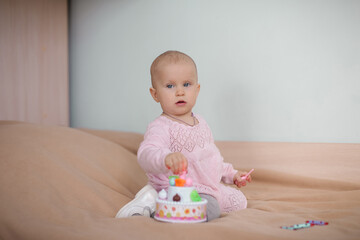 A one-year-old baby in a cute pink dress  sits on the bed