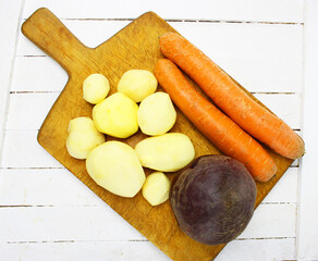 peeled round potatoes a huge pile of very large fresh and sweet carrots on a white wooden table. beautiful fresh market organic carrots in a large pile close-up full frame healthy food and healthy