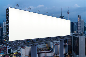 Obraz premium Blank white road billboard with KL cityscape background at night time. Street advertising poster, mock up, 3D rendering. Side view. The concept of marketing communication to promote or sell idea.