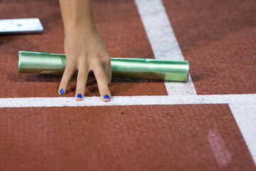 Starting position for relay race on the treatmill on the stadium. Green color baton in hand