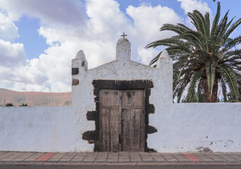 Obraz premium entrance of a typical white rural building with background palm trees and wooden door.Fuerteventura, Canary Islands, Spain.