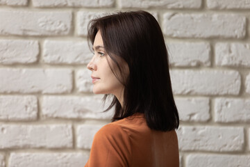 Side head shot pretty millennial brunette woman with shoulder length hair looking away, standing...