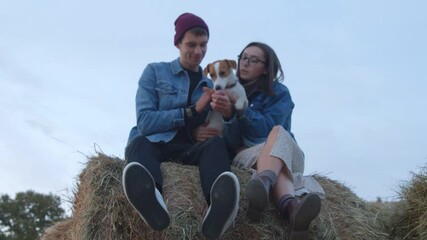 Young couple with jack russell terrier dog sits on haystack in evening