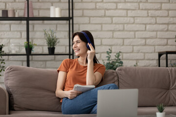 Fototapeta premium Distracted from distant study on computer happy female millennial student listening popular music in wireless modern tech headphones, enjoying break pause time, resting on cozy sofa at home.