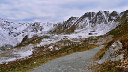 Fototapeta na wymiar Hiking path with trail marking leading through snow-covered Madrisa mountain range in Rätikon massif near Gargellen, Montafon, Austria, a popular tourist destination and hiking area, in autumn season.
