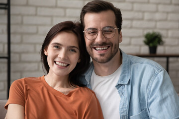Head shot portrait of happy loving affectionate millennial married family couple enjoying free leisure time together at home, holding video call web camera conversation or posing for photo indoors.