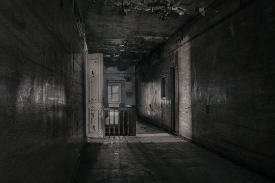 Dark gloomy corridor in an old abandoned building. Dirty wooden doors. Cracked on the walls. A window in the distance. Gloomy atmosphere.