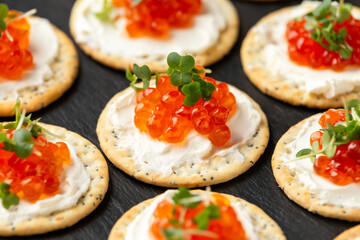 Salmon caviar and soft cheese savory crackers with sesame and poppy seeds served on black slate board