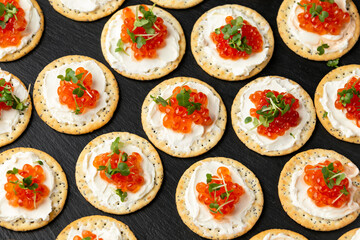 Salmon caviar and soft cheese savory crackers with sesame and poppy seeds served on black slate board