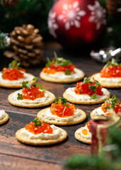 Salmon caviar and soft cheese savory crackers with decoration, gifts, green tree branch on wooden rustic table.