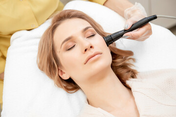 Obraz na płótnie Canvas Young woman receiving RF lifting electric facial massage for face skin