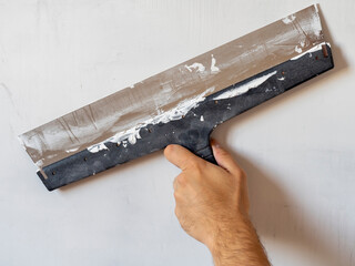 the hand of a worker with a long spatula that works on the wall. Interior work, construction concept