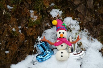 Figurine of a snowman in the winter forest. Next to Christmas boots.