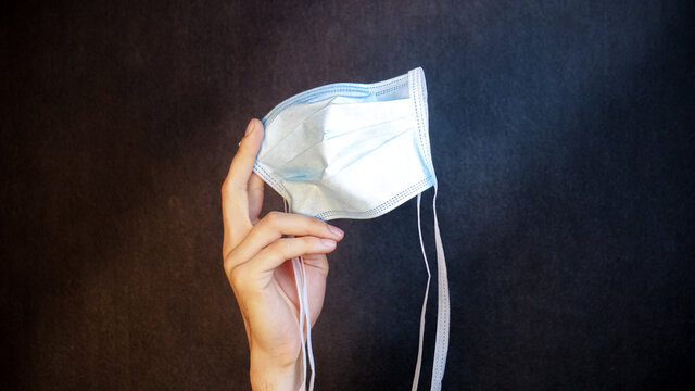 Light Blue Medical Mask In Hand On Black Background With Shadow And Light Lines In 3d For Viruses