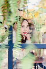 Naklejka premium Beautiful woman looking camera in a cafe viewed through glass with reflections