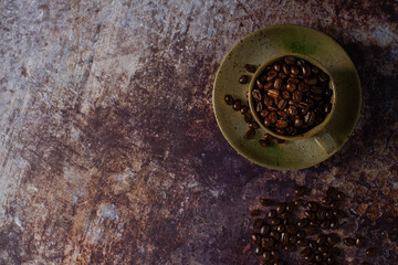 Top view above of Black coffee seed for morning menu in brown ceramic cup with coffee beans roasted on old rusty table background. Flat lay with copy space.
