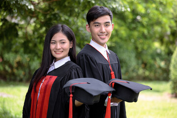 Two Asia college students wearing bachelor clothing and holding hat with red tassel