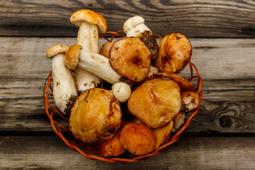 Freshly picked forest mushrooms in basket on rustic wooden table. Top view