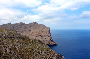 Seascape with soft clouds and blue sea stretching to the horizon. Beautiful view of a rocky promontory on the island of Mallorca, Spain.