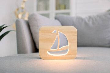 Close up of wooden night lamp with ship picture, on gray stylish sofa, at modern light home living room interior. Home decor and lamps. Wooden hand made accessories