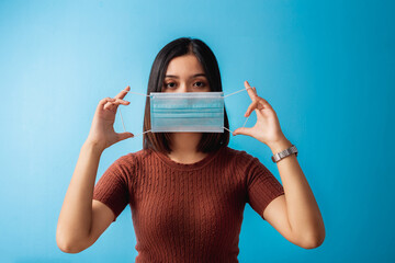 Young Asian woman showing how to wear a medical mask on blue background