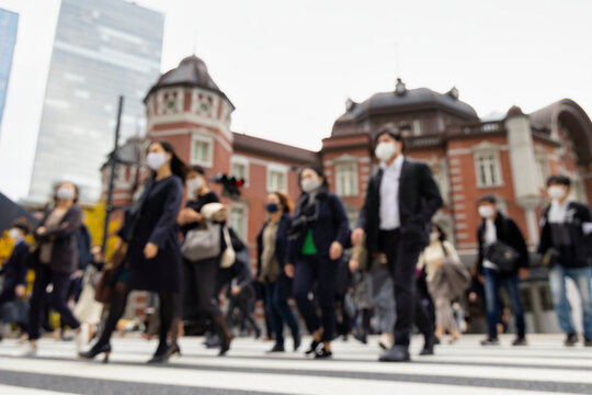 意図的にピントをぼかした東京駅前の横断歩道を渡るマスク姿のビジネスマンたち