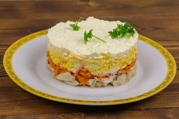 Tasty layered salad with chicken, carrot, eggs, cheese and mayonnaise on wooden table