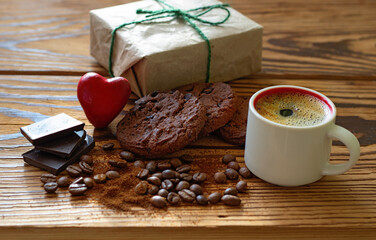 image of a cup with coffee, pieces of chocolate, coffee beans, chocolate chip cookies, stylized red heart and a holiday gift box
