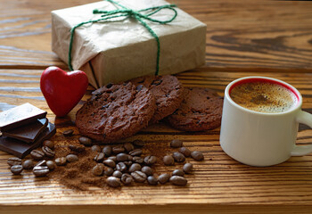 image of a cup with coffee, pieces of chocolate, coffee beans, chocolate chip cookies, stylized red heart and a holiday gift box