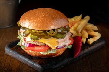 Bbq beef cheeseburger with pickled Jalapeno peppers, cheese and vegetables with French fries on the...