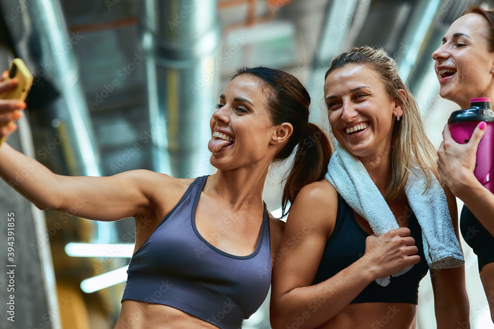 Wall mural having fun. group of three young beautiful and joyful sportive women taking selfie on smartphone whi