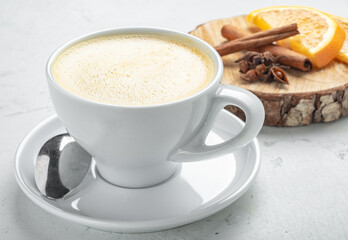Cappuccino coffee with orange flavor and cinnamon in a white mug on a white background.