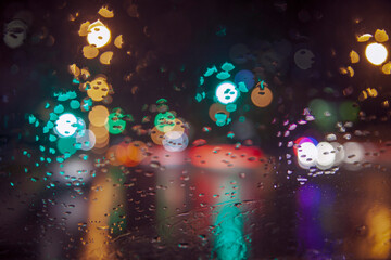 Obraz na płótnie Canvas Rainy weather, night city, raindrops through the glass, abstract background from the light of cars and traffic lights, defocus, rain drops on car glass in rainy night