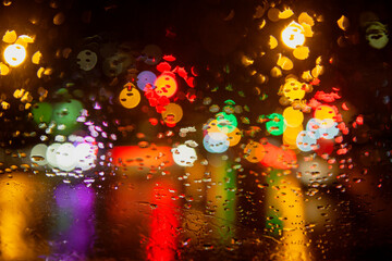 Rainy weather, night city, raindrops through the glass, abstract background from the light of cars...