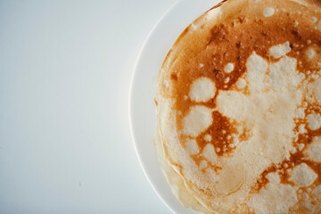 Traditional homemade thin pancakes without syrup, honey or jam on the white plate on the stone table. Close-up of prepared food. Fried or baked pastry for breakfast. Milan, Lombardy, Italy.