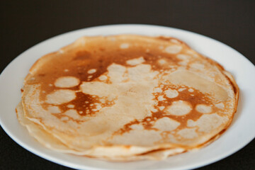 Traditional homemade thin pancakes without syrup, honey or jam on the white plate on the stone table. Close-up of prepared food. Fried or baked pastry for breakfast. Milan, Lombardy, Italy.