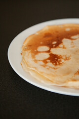 Traditional homemade thin pancakes without syrup, honey or jam on the white plate on the stone table. Close-up of prepared food. Fried or baked pastry for breakfast. Milan, Lombardy, Italy.