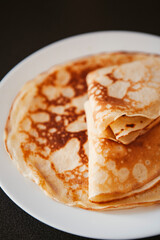 Traditional homemade thin pancakes without syrup, honey or jam on the white plate on the stone table. Close-up of prepared food. Fried or baked pastry for breakfast. Milan, Lombardy, Italy.