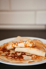 Traditional homemade thin pancakes without syrup, honey or jam on the white plate on the stone table. Close-up of prepared food. Fried or baked pastry for breakfast. Milan, Lombardy, Italy.