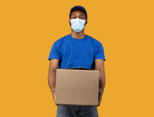 Black delivery man in medical mask holding cardboard box
