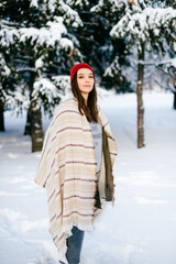 Fototapeta na wymiar Young attractive brunette girl covering with a warm cape posing in the snow forest