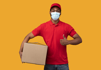 Fototapeta na wymiar Black delivery man in mask holding box, showing thumbs up