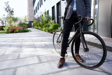 Cropped shot of stylish mature businessman standing with his bicycle near modern office building...