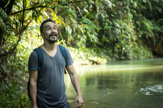 Hombre con barba en una expedición por la selva caminando junto a un rio con cara de sorprendido