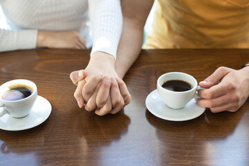 Female and man hands with cups of coffee on the background of a wooden table. Relationship concept during travel vacation. Focus on together hands