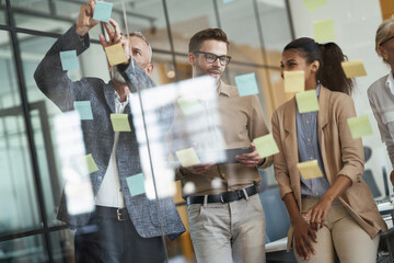 Group of multiracial coworkers standing in the modern office and putting colorful sticky notes on a...