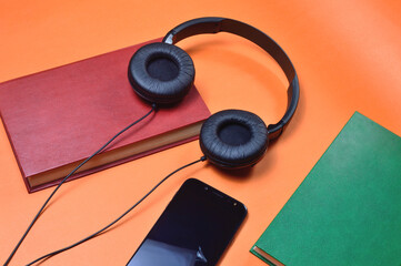 book, smartphone, headphones on an orange background. audiobook. hobby. free time. recreation. literature.