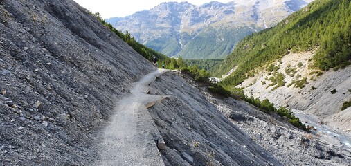 bicycle rider on gravel road path in a steep valley in the alps, summer 2020